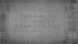 An inspirational quote by Ben Okri is etched onto a stone wall. The quote reads 'Our future is greater than our past' and is set in a serif font. The background is textured stone, giving a sense of permanence and strength.