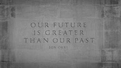 An inspirational quote by Ben Okri is etched onto a stone wall. The quote reads 'Our future is greater than our past' and is set in a serif font. The background is textured stone, giving a sense of permanence and strength.
