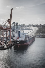 A large cargo ship loaded with chemical containers at a busy industrial port.