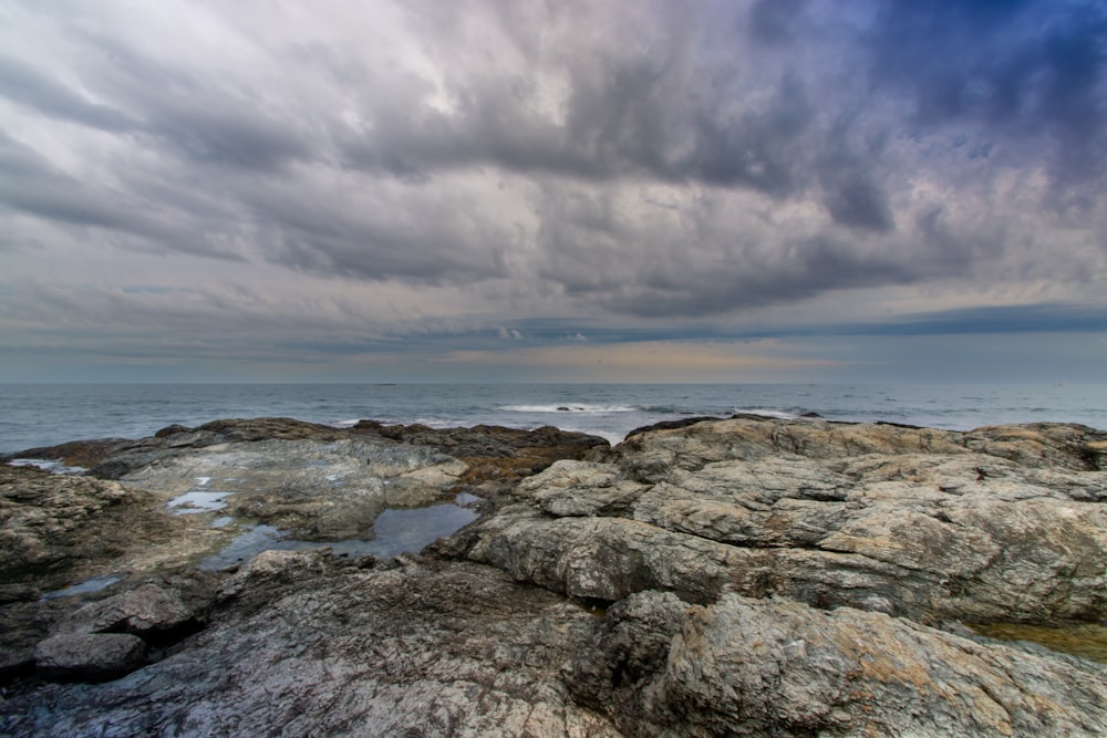a cloudy sky over the ocean with rocks in the foreground