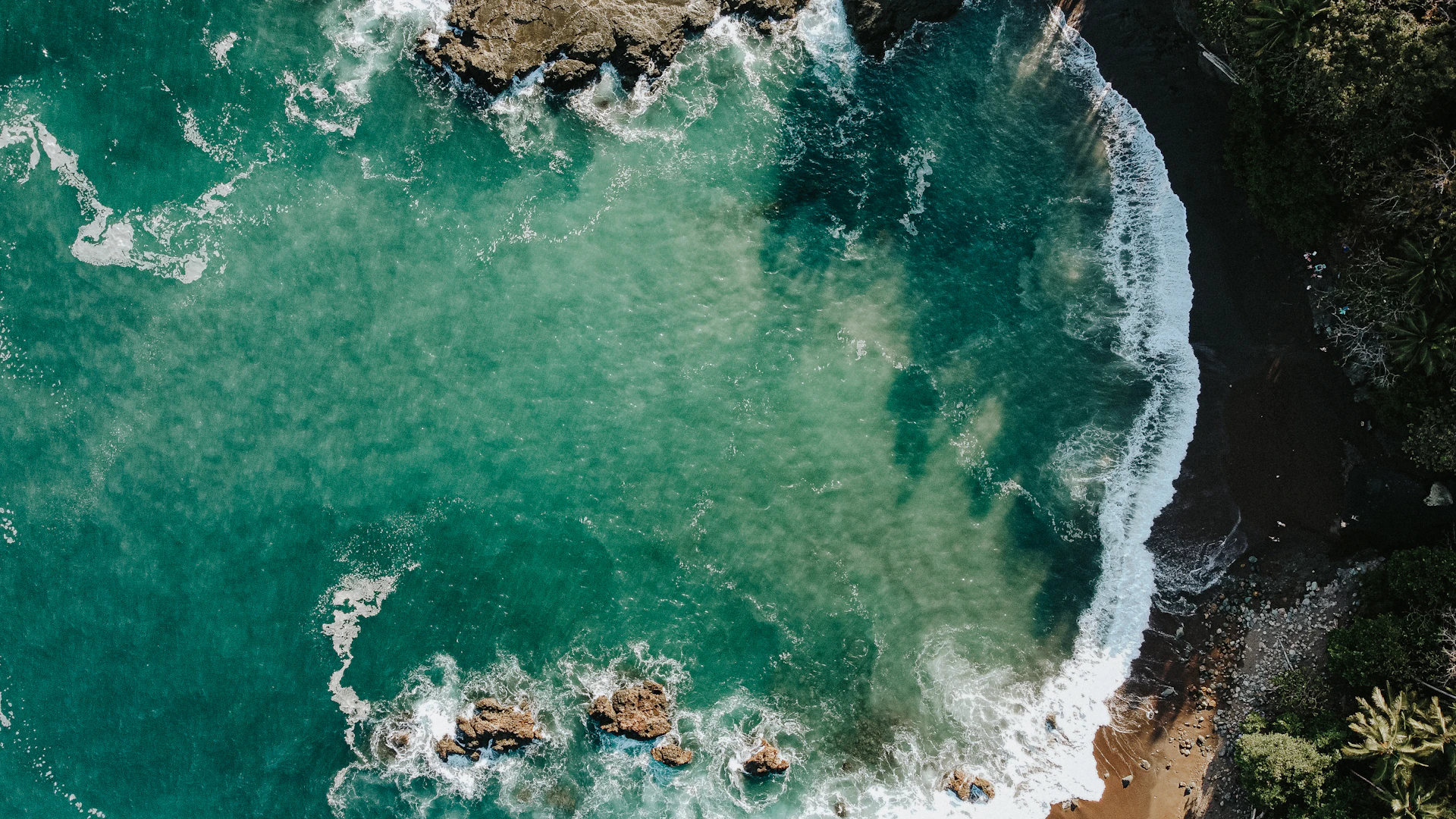 an aerial view of the ocean with waves crashing on the rocks