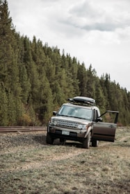 A rugged SUV with a roof rack, parked near a forest trail under bright blue skies.