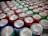A collection of colorful soda cans is closely packed together, showcasing a variety of brands and flavors. The tops of the cans are prominently displayed, with silver pull tabs visible. The colors range from red, green, blue, to silver, indicating a diverse selection. Some cans display nutrition facts labels, hinting at the variety of options available.
