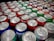 A collection of colorful soda cans is closely packed together, showcasing a variety of brands and flavors. The tops of the cans are prominently displayed, with silver pull tabs visible. The colors range from red, green, blue, to silver, indicating a diverse selection. Some cans display nutrition facts labels, hinting at the variety of options available.