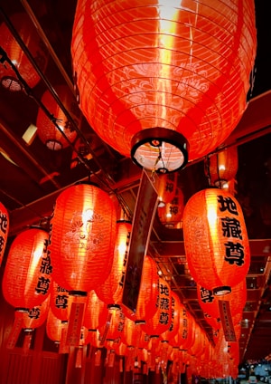 A series of vibrant red paper lanterns with black characters hang closely together, creating a warm and festive atmosphere. The lanterns are intricately decorated and illuminated from within, casting a soft glow.
