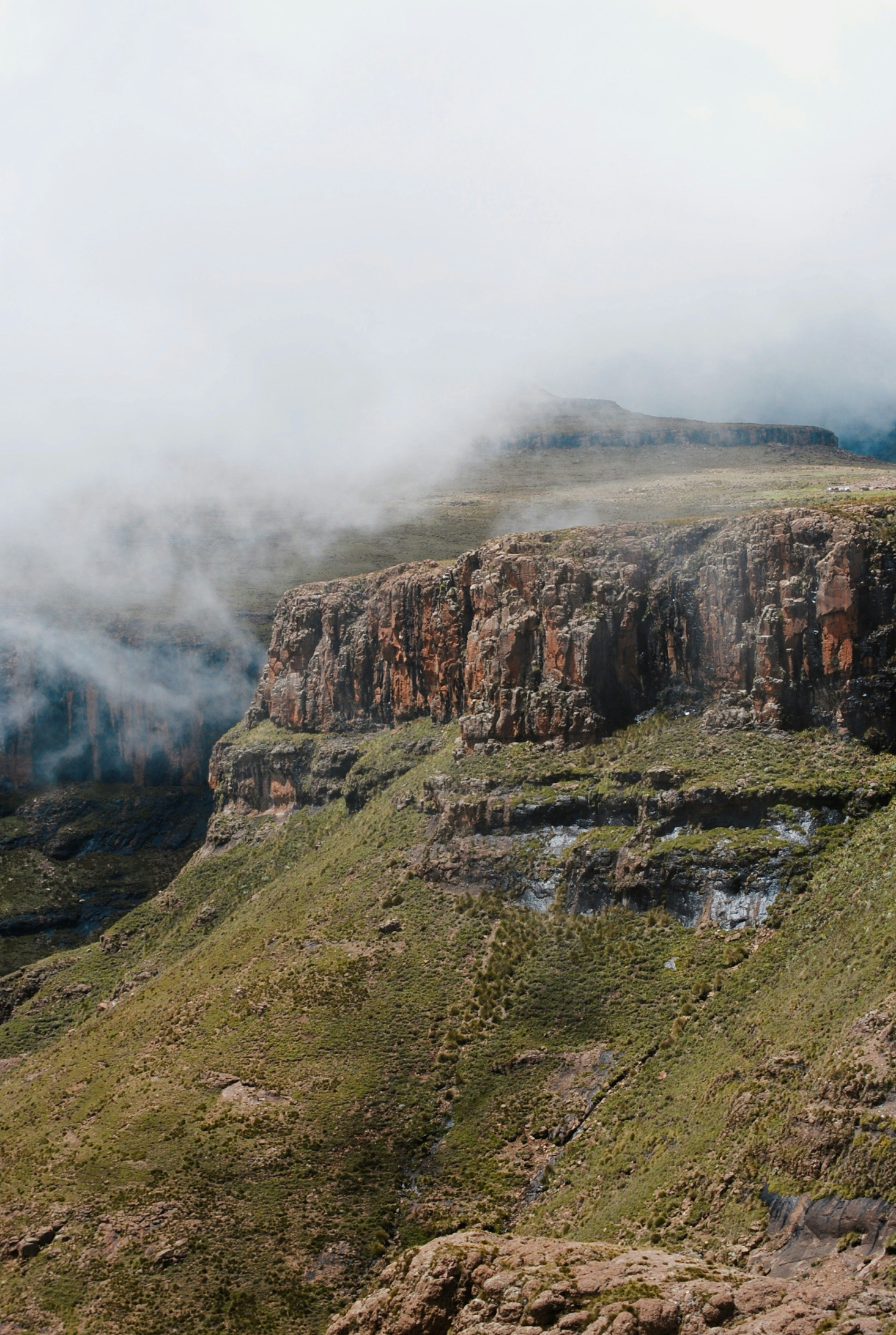 a rocky cliff with a small patch of grass in the foreground