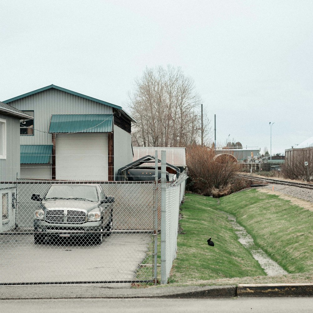 a car parked in front of a house behind a chain link fence