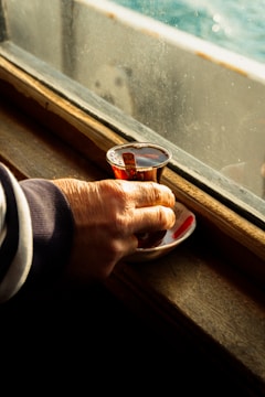 Hands holding a cup of herbal tea near a window.