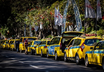 A row of bright yellow taxis waiting near a busy city square at dusk.
