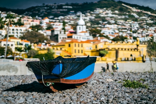 a blue and black boat sitting on top of a rocky beach