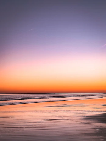 A vibrant beach sunset with golden skies and calm blue waters, inviting relaxation.