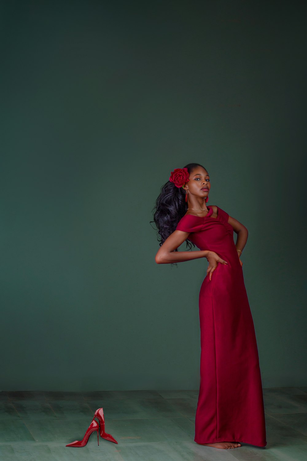 a woman in a red dress standing next to a pair of red shoes