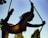 A silhouetted figure with curly hair is performing an acrobatic pose on a rope against a clear sky, with one leg extended gracefully behind. The background shows blurred green foliage.