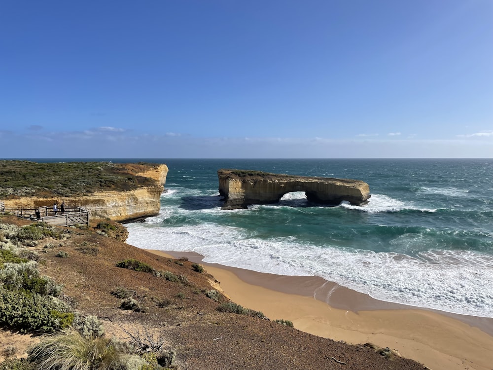 a large rock sticking out of the ocean next to a beach