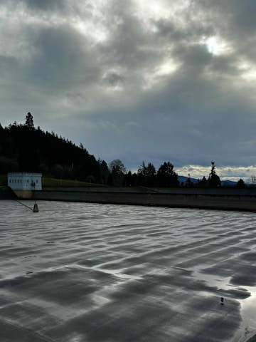 Technicians applying waterproof coating carefully on a large commercial floor site under cloudy skies.