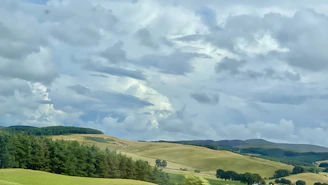 A wide landscape shot of rolling hills under a dramatic cloudy sky.