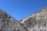 Rocky mountains with a steep, rugged terrain under a clear blue sky. High-tension power lines are visible running across the mountain landscape.
