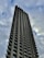 A tall, modern skyscraper extends into a cloudy sky, featuring a distinct pattern of vertical lines and rows of windows. The building has a robust and angular architectural design, creating a striking silhouette against the overcast backdrop.