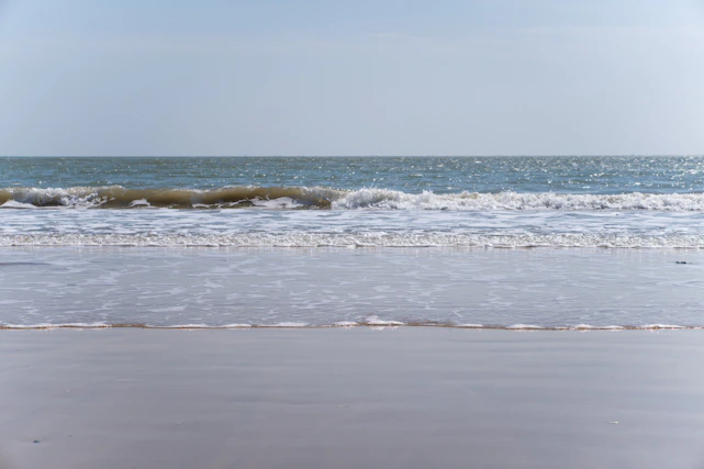 A calm ocean wave gently rolling onto a sandy shore under a clear sky, symbolizing smooth communication and flow
