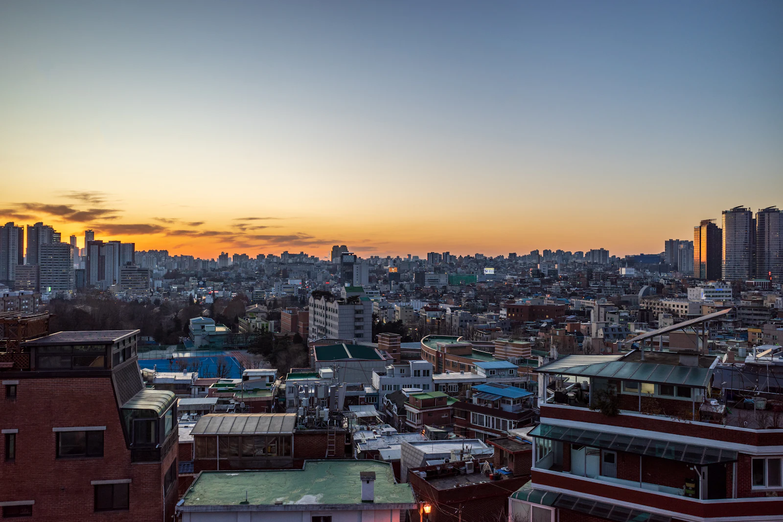 Seoul rooftops and apartment towers under an orange sunset sky, a city where a Korea eSIM keeps Naver Map running