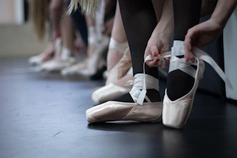Close-up of hands tying ballet shoes, highlighting preparation and care.