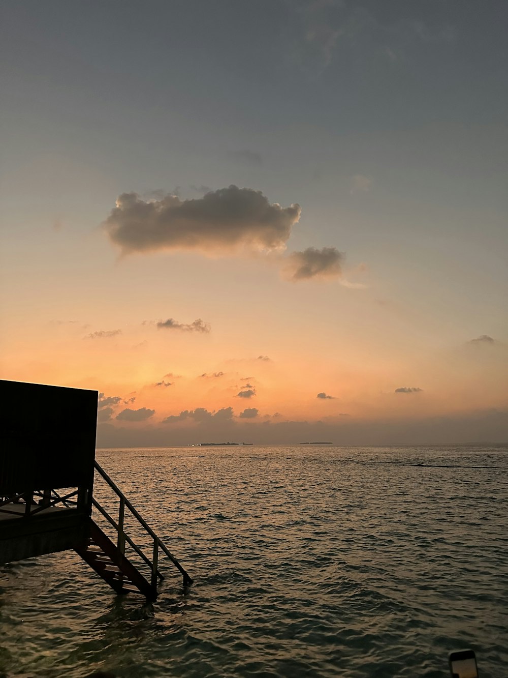 the sun is setting over the ocean with a dock in the foreground