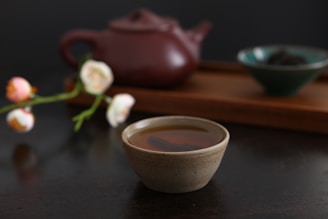 a cup of tea next to a teapot and a flower