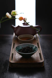 A steaming cup of black tea on a traditional Arabic tray with loose tea leaves beside it.