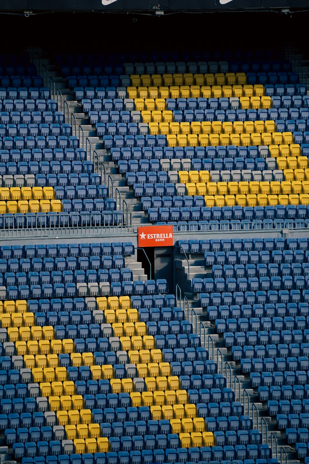 un stade avec des sièges bleus et jaunes et un panneau rouge