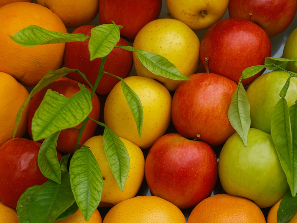 a pile of oranges and apples with leaves on them