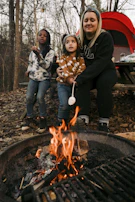 A family gathered around a campfire roasting marshmallows as twilight sets in.