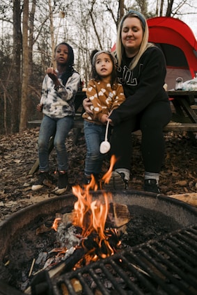 A family gathered around a campfire, testing survival gear together in a forest setting.
