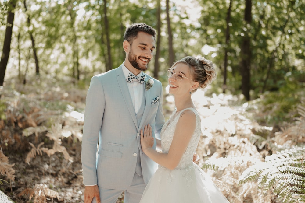 a bride and groom smile as they stand in the woods