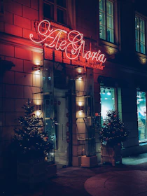 A welcoming entrance of Ampelos with red and white signage glowing softly in the evening.