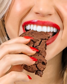 a woman eating a chocolate cookie with red lipstick