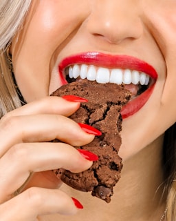 a woman eating a chocolate cookie with red lipstick