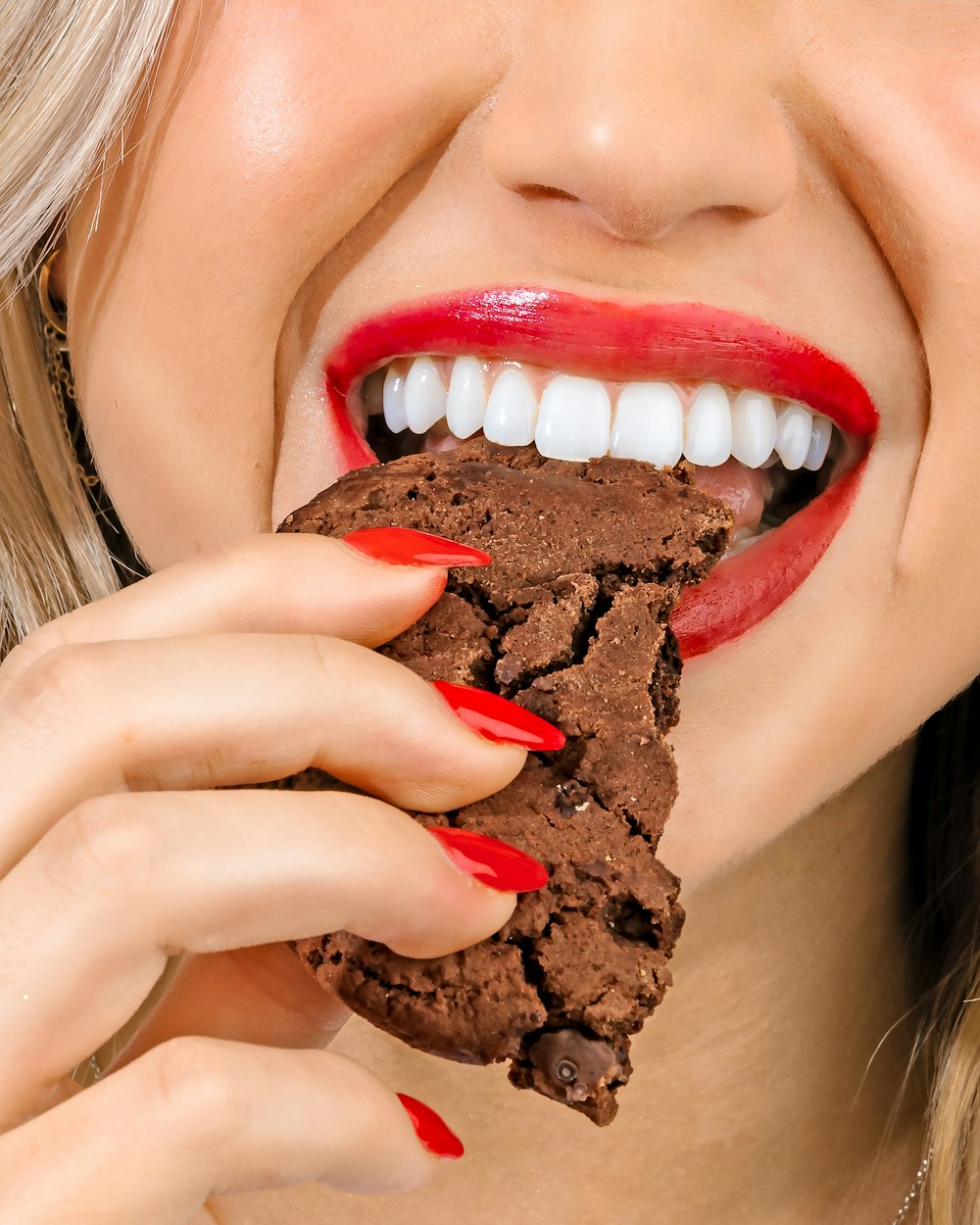 a woman eating a chocolate cookie with red lipstick