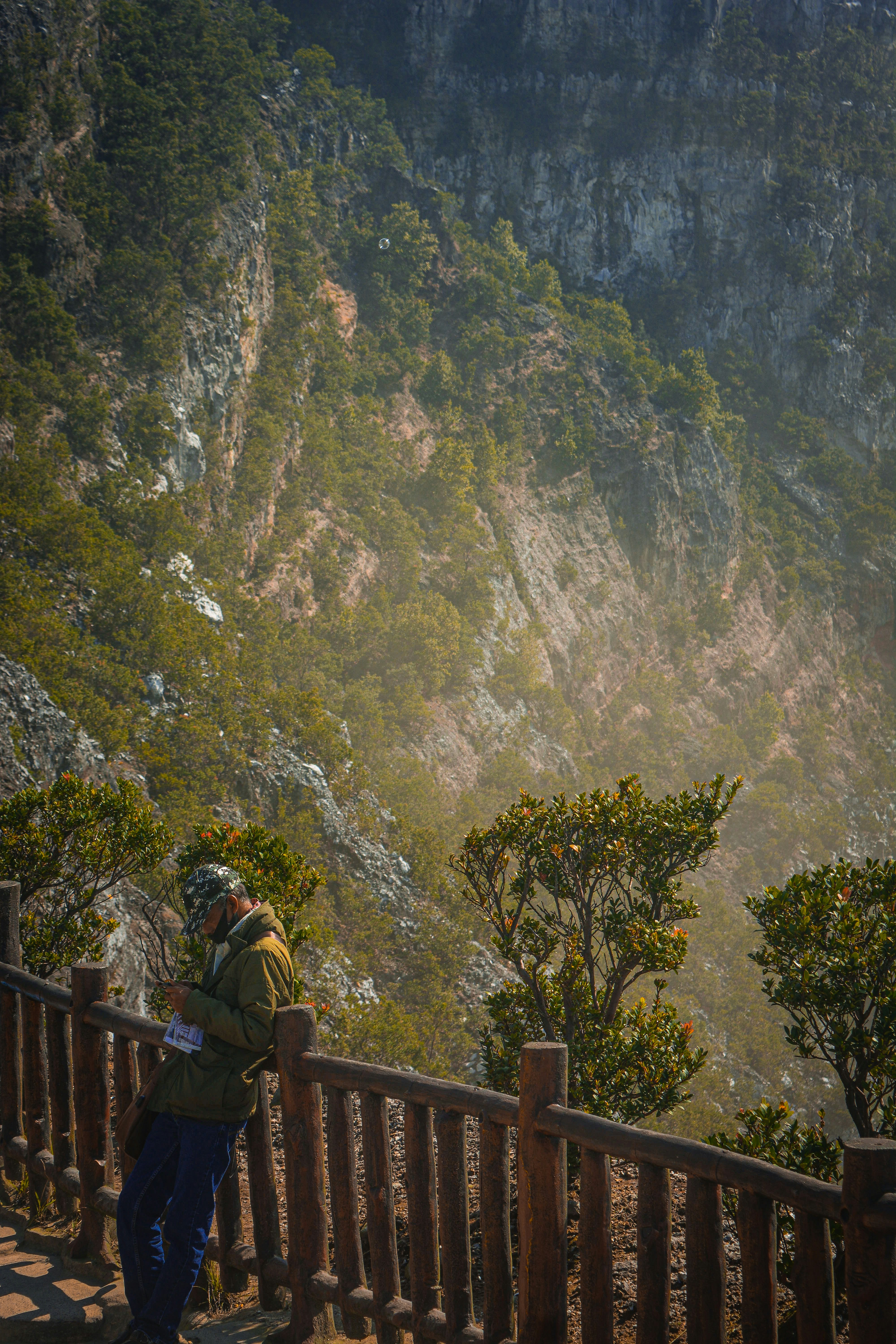 um homem em pé no topo de uma varanda de madeira ao lado de uma encosta verde exuberante