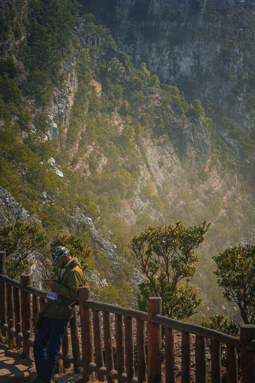 a man standing on top of a wooden balcony next to a lush green hillside