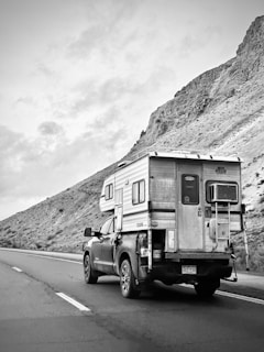 An Alaskan-made slide-in camper mounted on a pickup truck driving through a forested landscape
