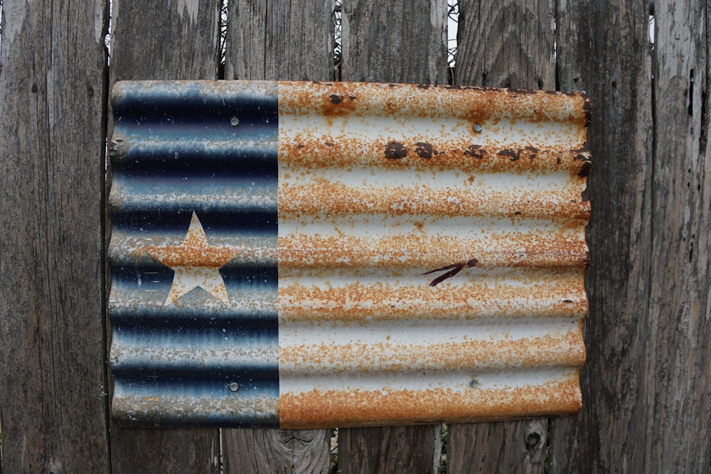 a rusted metal flag hanging on a wooden fence