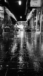 A black and white photo of a rain-soaked street reflecting neon lights at dusk.