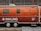 A vintage Airstream trailer with an orange exterior is parked in front of an industrial building with large grid-like windows. The trailer features the word 'INKLING' in bold white letters and some additional text, suggesting it is associated with a brand or company. A website URL is also visible on the trailer.
