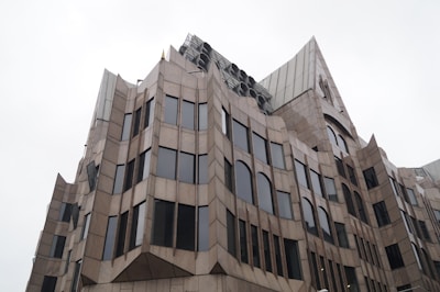 A modern, multi-story building with a unique geometric facade featuring numerous large windows. The structure has sharp lines and angular forms that create a distinctive architectural style.