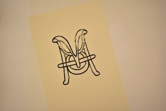 An intricately designed monogram featuring the letters 'M' and 'A' intertwined in a decorative style, printed in black on a cream-colored background.