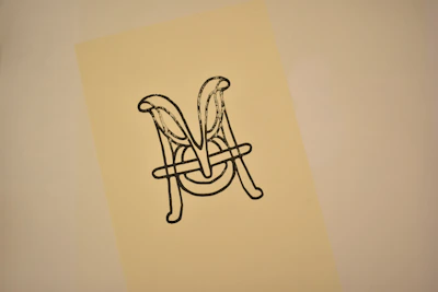 Close-up of a sophisticated monogram logo featuring the letter 'n' and a feather in navy and gold.