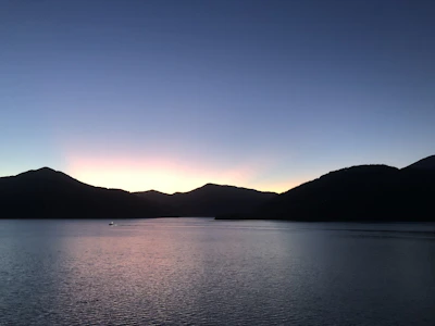A serene lakeside scene at dusk, with calm water reflecting muted terracotta and dusty blue skies.