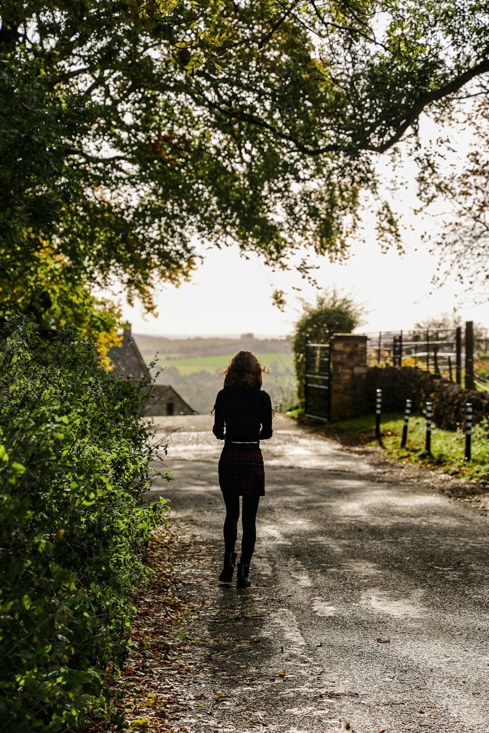 a woman walking down a dirt road next to a lush green field