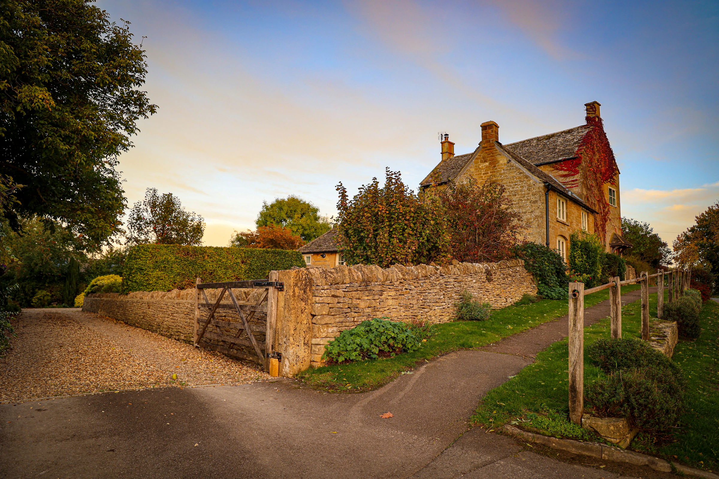 Traditional stone house behind a stone boundary wall and a gate. Reference photograph; not the project described.