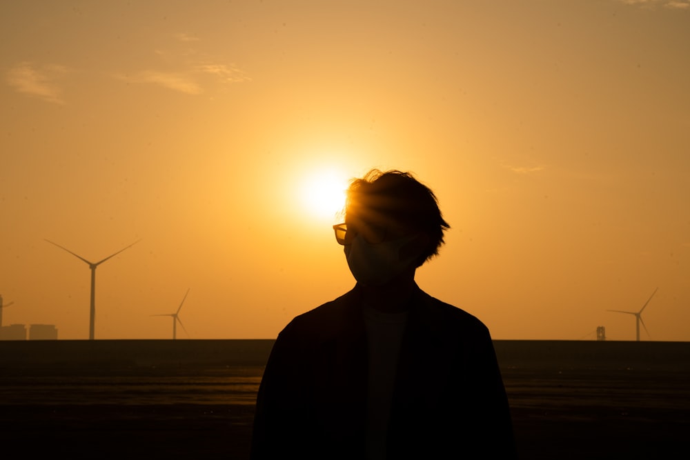 a man standing in front of a sunset with windmills in the background